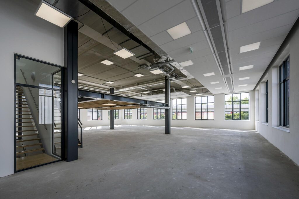 Spacious industrial-style office space with large windows, exposed ceilings, and a mezzanine level on Paul van Vlissingenstraat.